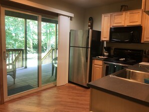 A kitchen with a refrigerator, microwave, stove, and a view of a deck through a sliding glass door.