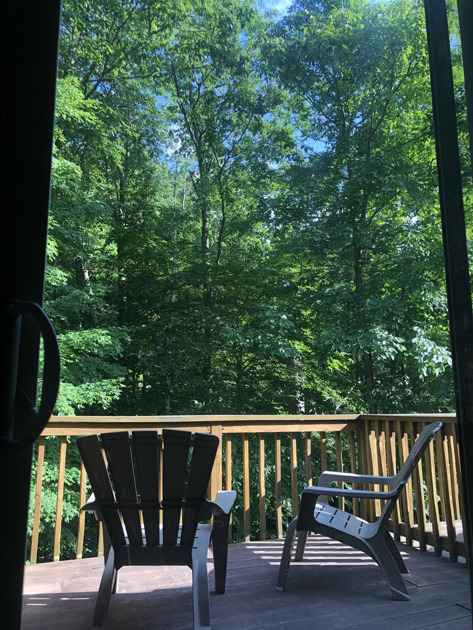 A wooden deck with two Adirondack chairs facing a forested area.