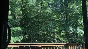 A wooden deck with two Adirondack chairs facing a forested area.