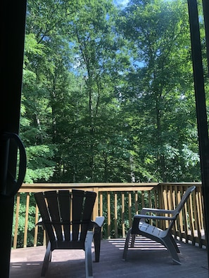 Eine Holzterrasse mit zwei Adirondack-Stühlen, die auf einen bewaldeten Bereich ausgerichtet sind.