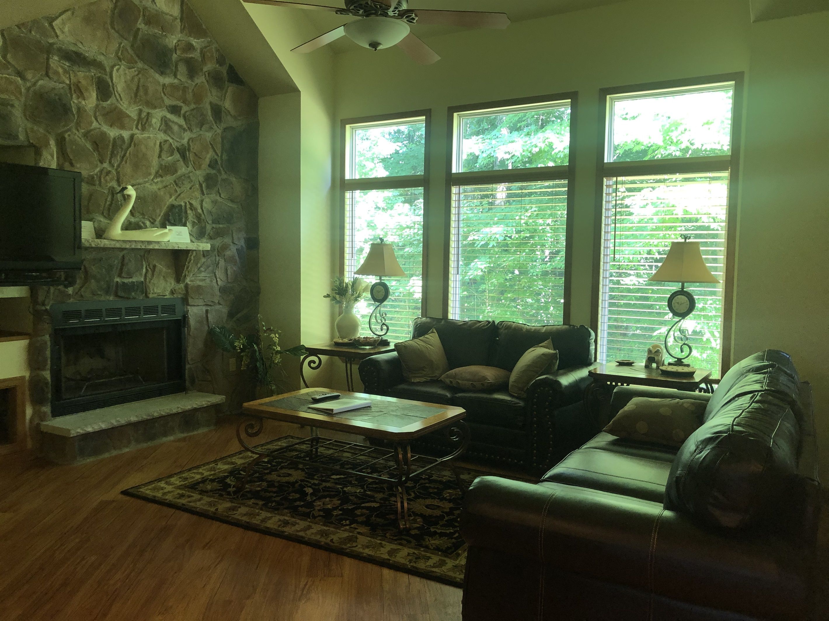 A living room with a stone wall, fireplace, leather sofas, a coffee table, and large windows with blinds.