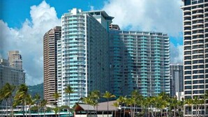Un hôtel de grande hauteur doté de nombreux balcons, avec une plage au premier plan et des palmiers.