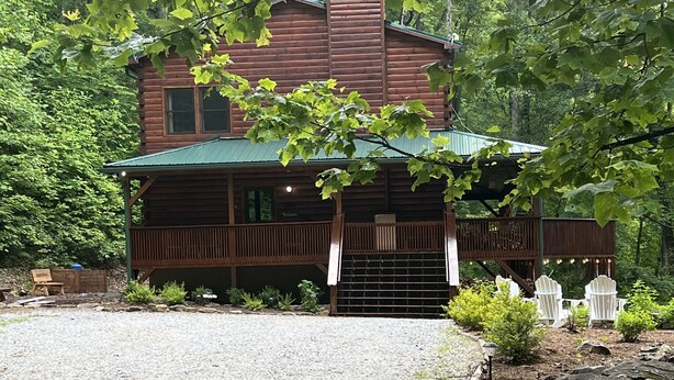A rustic log cabin with a porch and a gravel driveway.