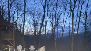 A deck with four Adirondack chairs and a wooden structure in the background.