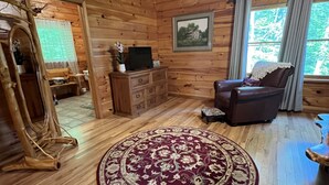A wooden cabin interior with a round patterned rug, wooden furniture, a television, and a framed picture on the wall.