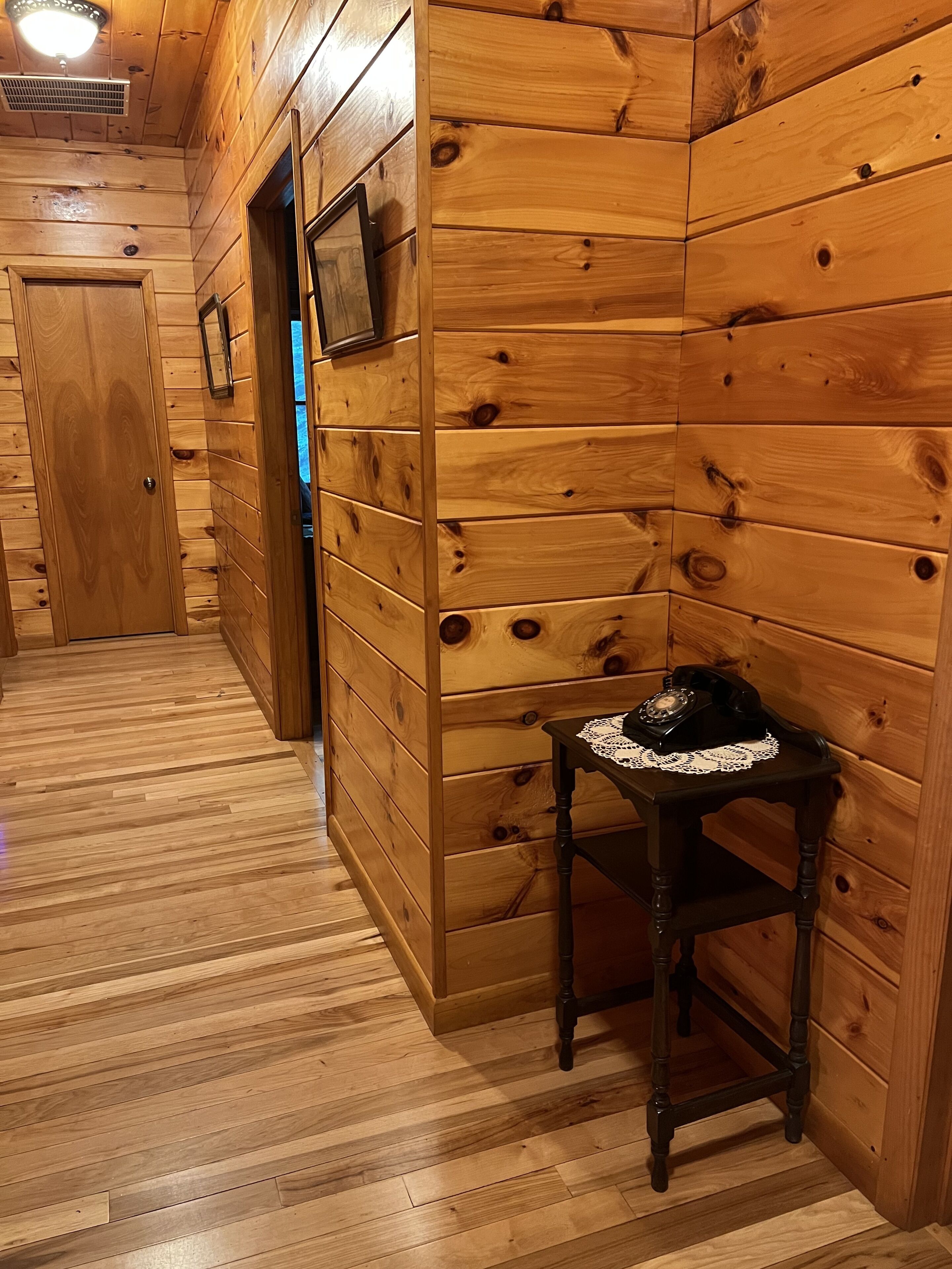 Un pasillo con paneles de madera, una puerta, una mesita con un teléfono y un marco de cuadro en la pared.