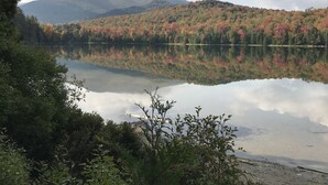 Un lago tranquilo con reflejos de árboles y montañas, rodeado de abundante vegetación.