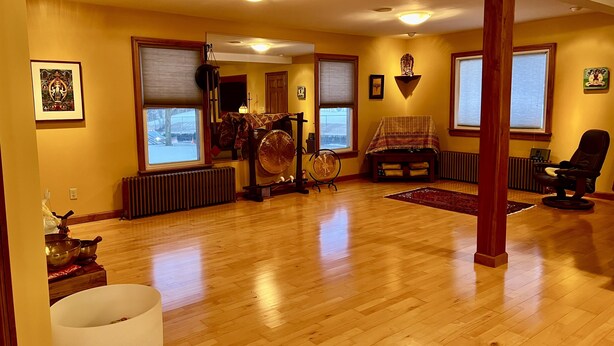 A spacious living room with wooden flooring, large windows, and a fireplace. - Village Hideaway, 1 bdrm efficiency, private entrance. On the Rail Trail. (Saranac Lake)