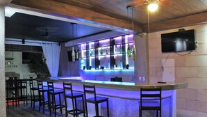 Eine Bar mit Theke, Barhocker und einem an der Wand befestigten Fernseher.