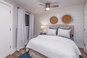 Een slaapkamer met een bed, een plafondventilator, een nachtkastje met een lamp en twee decoraties aan de muur.