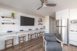 Een moderne keuken met een grote koelkast, magnetron en fornuis. Er staan houten krukken en een grijze bank.