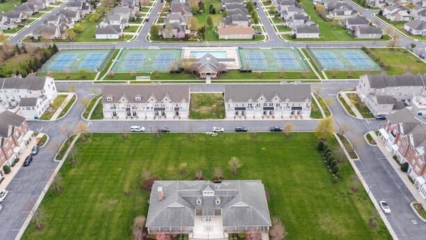 An aerial view of a residential area with a large building featuring a central courtyard, tennis courts, and a swimming pool.
