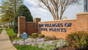 A brick wall with "The Villages of Five Points" sign, surrounded by grass and flowers.