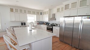 Una cocina moderna con armarios blancos, una isla grande, electrodomésticos de acero inoxidable y piso de madera.