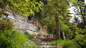 A wooden deck with steps leading to a house surrounded by lush greenery and trees. - Comfortable luxury suite with epics views, on the Beach, Sunshine Coast (Halfmoon Bay)
