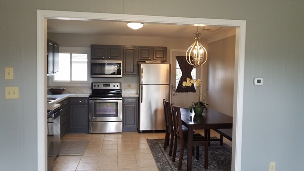 A modern kitchen with stainless steel appliances, a dining area with a table and chairs, and a chandelier. - Cozy 3 Bedroom Ranch No steps (Tiffin)