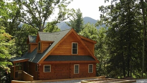 Une cabane en rondins avec un toit à forte pente, un porche à l’avant et une petite terrasse.