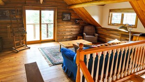 A log cabin interior with a wooden ceiling, a large window, a chair, a table, and a lamp. - Mountain Log Home Close to Historic Downtown Bozeman & Bridger Bowl. (Bozeman)