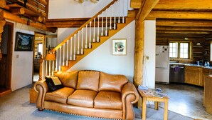 A spacious living room with a leather sofa, a wooden staircase, and a kitchen area. - Mountain Log Home Close to Historic Downtown Bozeman & Bridger Bowl. (Bozeman)