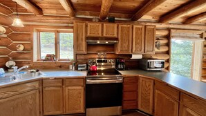 A rustic cabin kitchen with wooden cabinets, a stainless steel stove, a microwave, and a sink. - Mountain Log Home Close to Historic Downtown Bozeman & Bridger Bowl. (Bozeman)