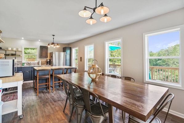 A spacious kitchen with a large wooden table, bar stools, and a hanging light fixture.