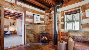 A cozy room with a brick fireplace, a sofa, and a bed. - ONE OF A KIND HISTORIC LOG CABIN ON 10+ ACRES IN HOCKING HILLS (Sugar Grove)
