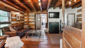 A log cabin interior with a leather sofa, a television, and a wooden ceiling. - ONE OF A KIND HISTORIC LOG CABIN ON 10+ ACRES IN HOCKING HILLS (Sugar Grove)