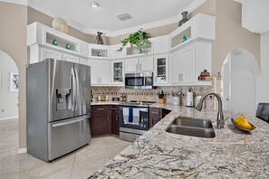 A modern kitchen with a stainless steel refrigerator, a microwave, an oven, and a sink with a marble countertop.