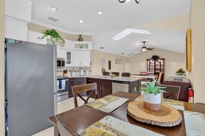 Une cuisine moderne avec des meubles blancs, un réfrigérateur et un coin repas comprenant une table et des chaises en bois.