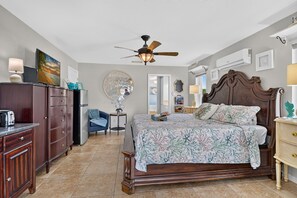 Une chambre à coucher avec un lit, une commode, une chaise, un ventilateur de plafond et une fenêtre.