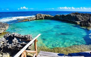 A clear blue sea with rocky formations and a wooden chair. - Isla Mujeres Condo #17 at Nautibeach- Playa Norte Beachfront, Pool, Walk to Town (Isla Mujeres)