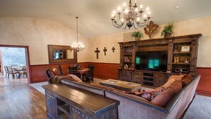 A spacious living room with a large sectional sofa, a wooden entertainment center, and a chandelier. - Blanco Rapids Ranch (Wimberley)