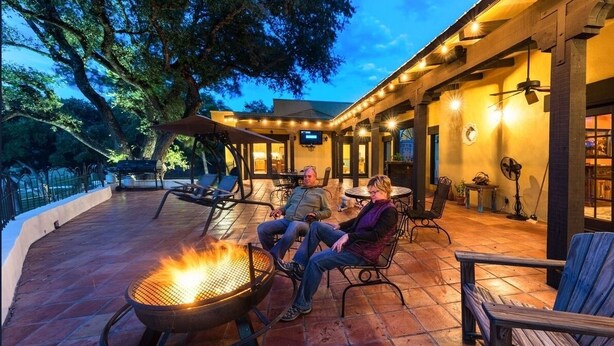 An outdoor patio area with a fire pit, seating, and a covered section with tables and chairs. - Blanco Rapids Ranch (Wimberley)