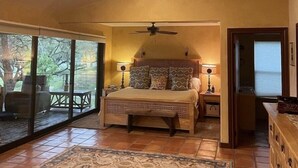 A bedroom with a bed, a ceiling fan, a nightstand, and a view through a sliding glass door to an outdoor patio. - Blanco Rapids Ranch (Wimberley)