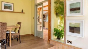 Une pièce comprenant une table à manger et des chaises, une porte donnant sur une autre pièce, et des tableaux encadrés accrochés au mur.