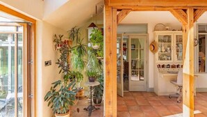 Une pièce avec un plafond en bois, un bureau et un meuble avec des portes en verre. On y trouve plusieurs plantes en pot et une plante suspendue.