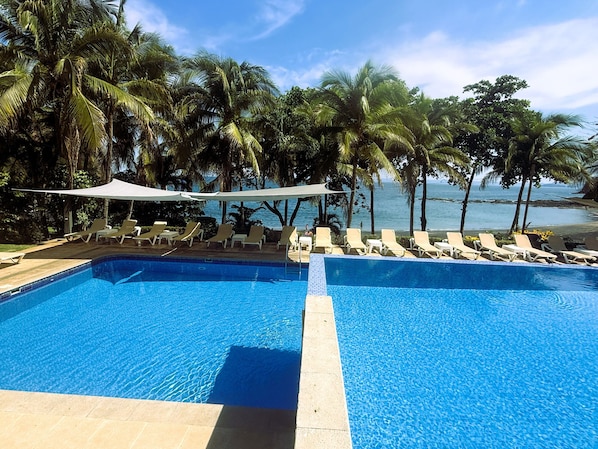 A pool with lounge chairs and palm trees, overlooking a beach.