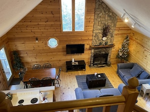 A cozy cabin interior with a stone fireplace, wooden walls, a dining area, and a living room with a sofa and a television.