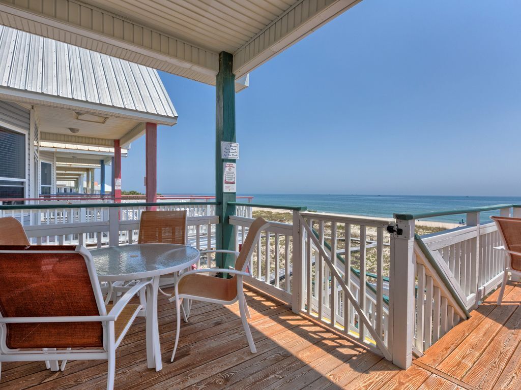 A wooden deck with a glass table and chairs, overlooking a beach.