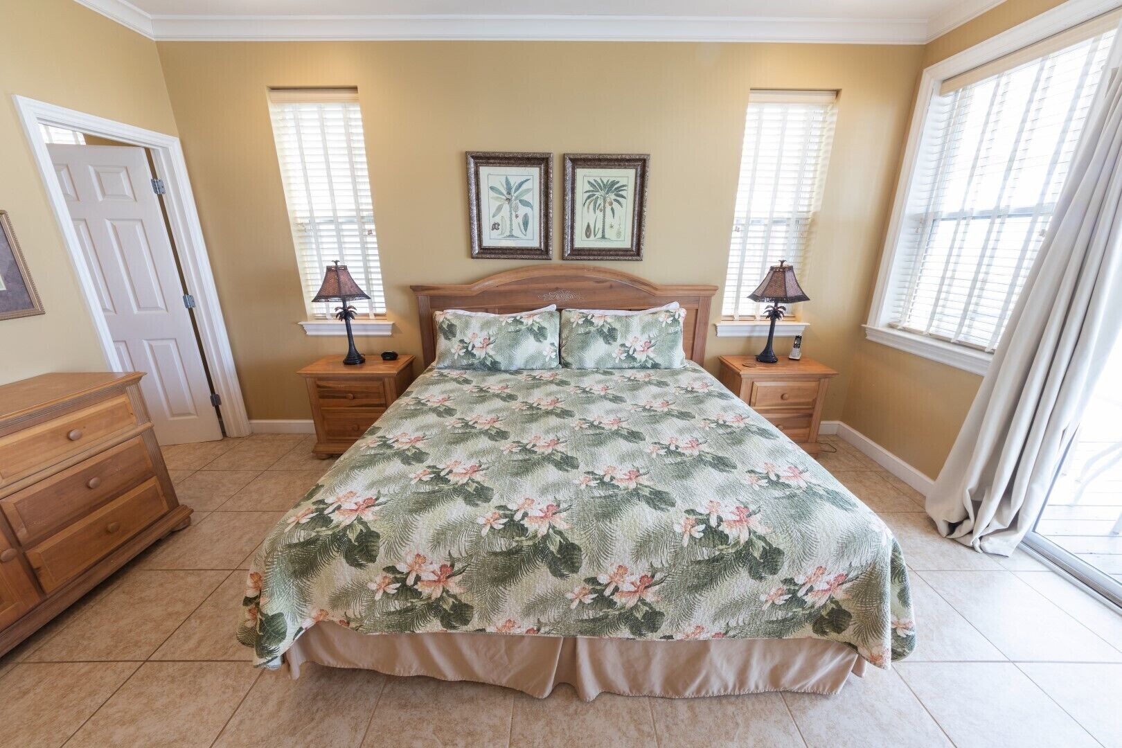 A bedroom with a floral bedspread, two bedside lamps, a wooden headboard, and a door.