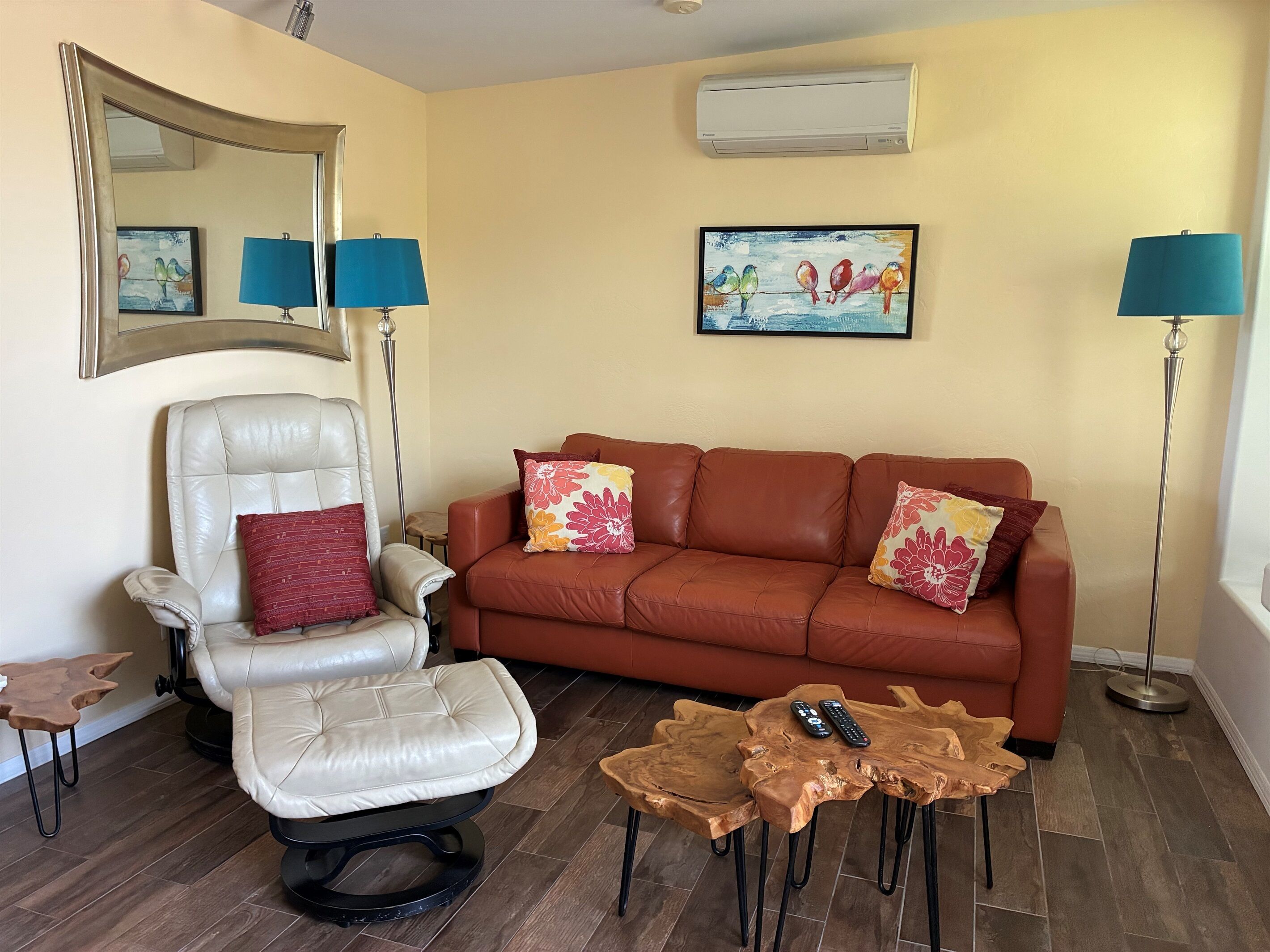 A living room with a white leather chair, a brown leather sofa, a wooden coffee table, and two floor lamps.