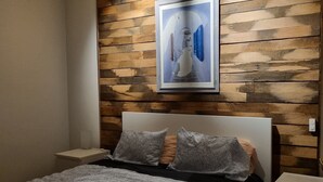 Een moderne slaapkamer met een houten paneelwand, een groot bed met beddengoed met een patroon en een lijstwerk met kunst boven het bed.