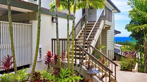 Una escalera conduce a un balcón con vista al océano, rodeado de plantas tropicales.
