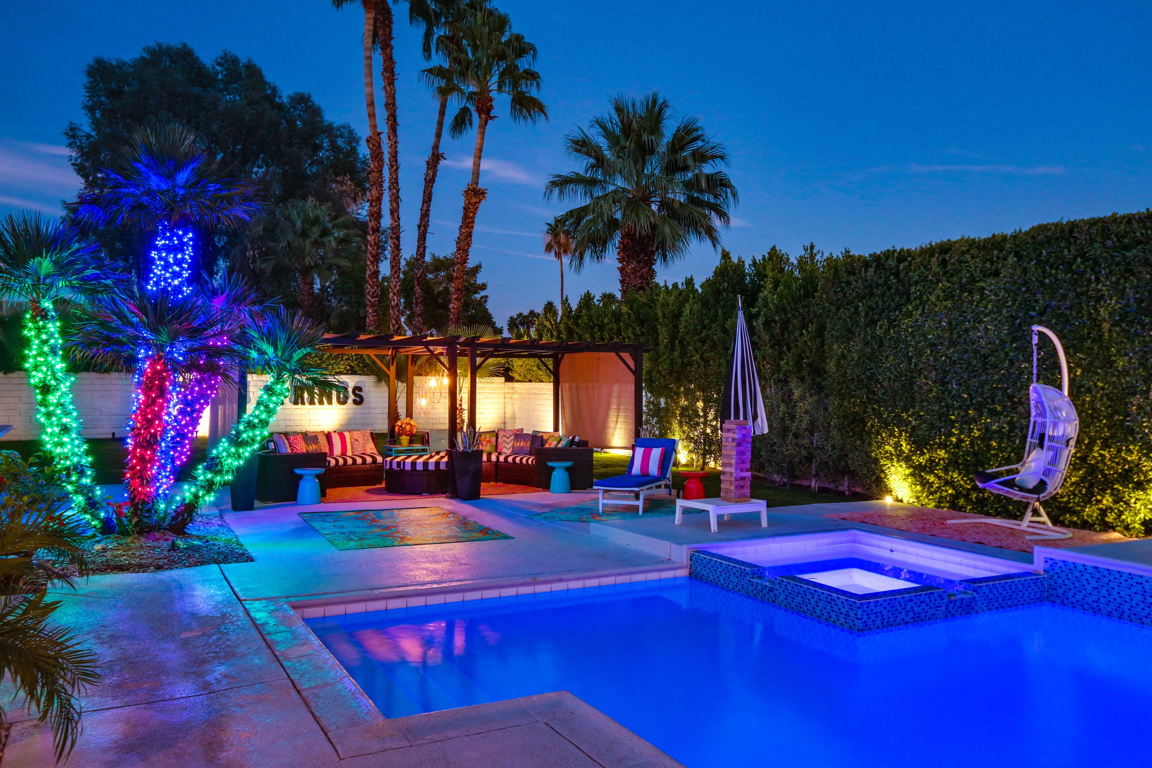 A pool area with a lounge, palm trees, and a well-lit outdoor seating area.