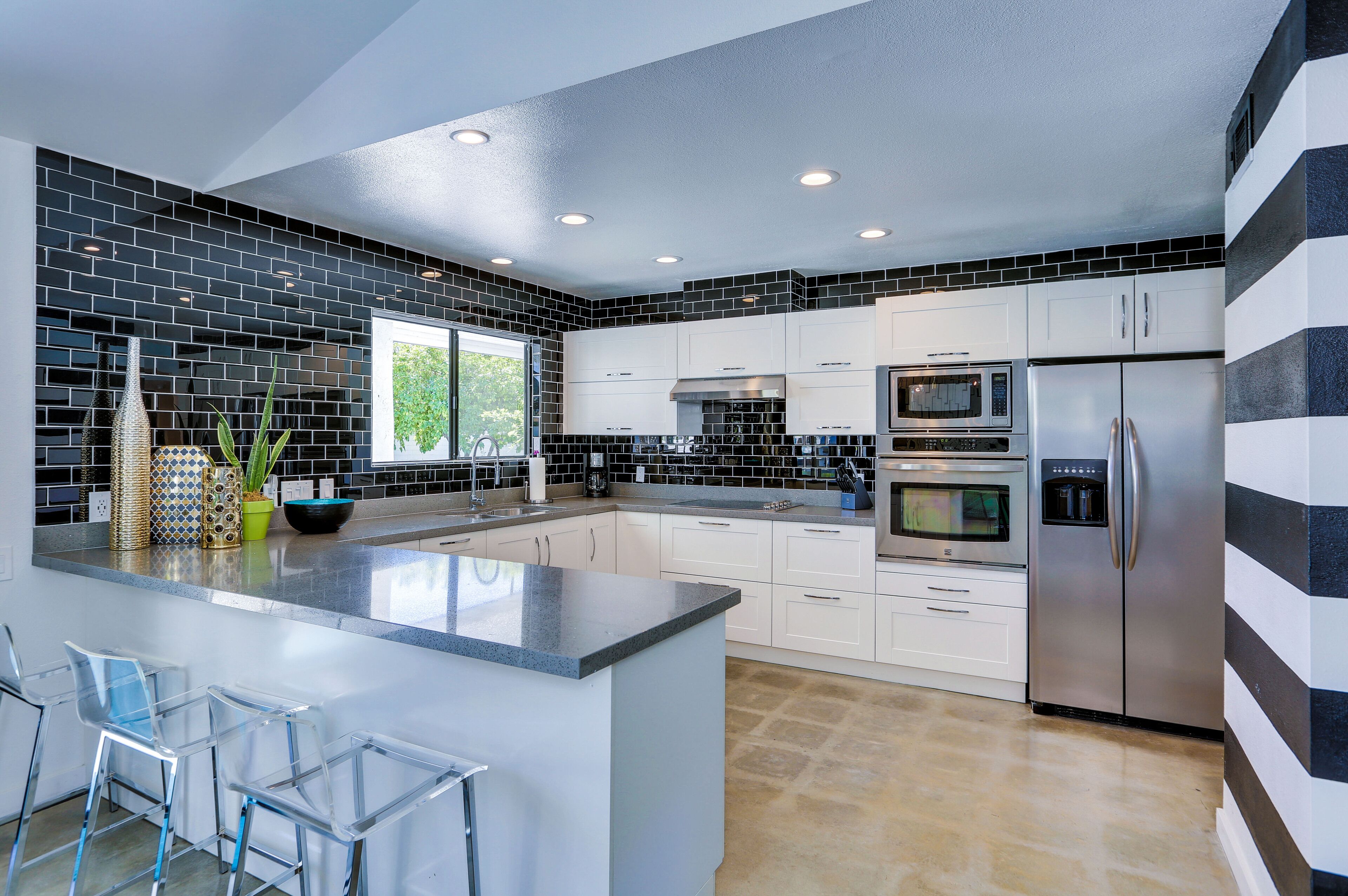 A modern kitchen with a central island, stainless steel appliances, and a black and white striped accent wall.