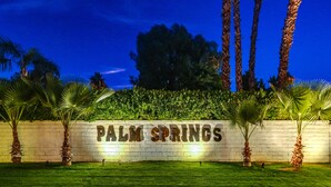 Et veloplyst skilt med teksten "PALM SPRINGS", forgrunden er græsset, og der er palmer.
