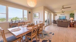 Een ruime woonkamer met een houten eettafel, stoelen en een groot raam met uitzicht op de omgeving.