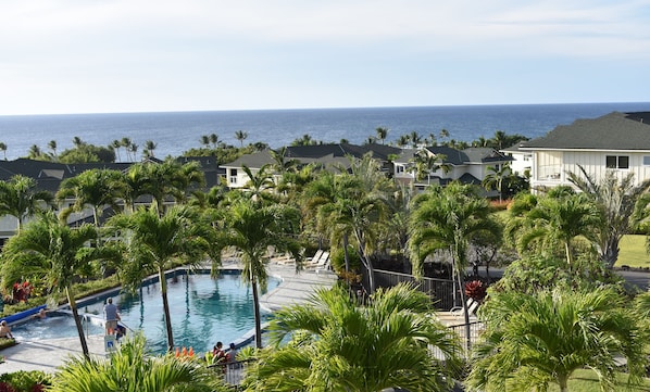 Ein Poolbereich mit Blick aufs Meer, umgeben von Palmen und Häusern.