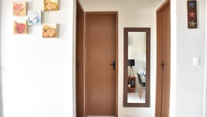 A hallway with a wooden door, a mirror, and a wall with floral artwork. - Cozy house with Wi-Fi and air conditioning. (Tamandaré)