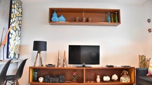 A modern living room with a flat-screen TV, wooden shelves, and various decorative items. - Cozy house with Wi-Fi and air conditioning. (Tamandaré)